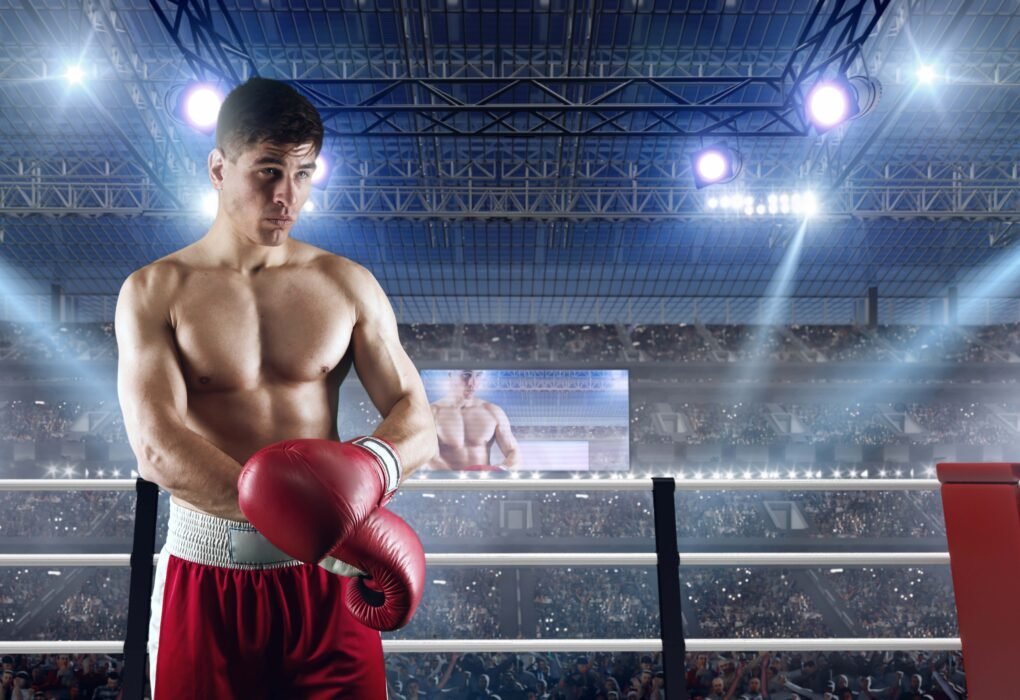 A professional boxer in a red and white uniform standing in a brightly lit boxing ring, preparing for a match with a stadium crowd in the background.