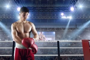 A professional boxer in a red and white uniform standing in a brightly lit boxing ring, preparing for a match with a stadium crowd in the background.